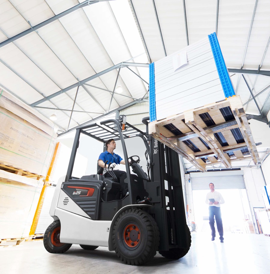 a man driving a Bobcat forklift in a warehouse holding a box