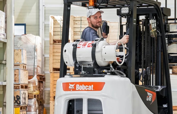 a man driving a white Bobcat forklift